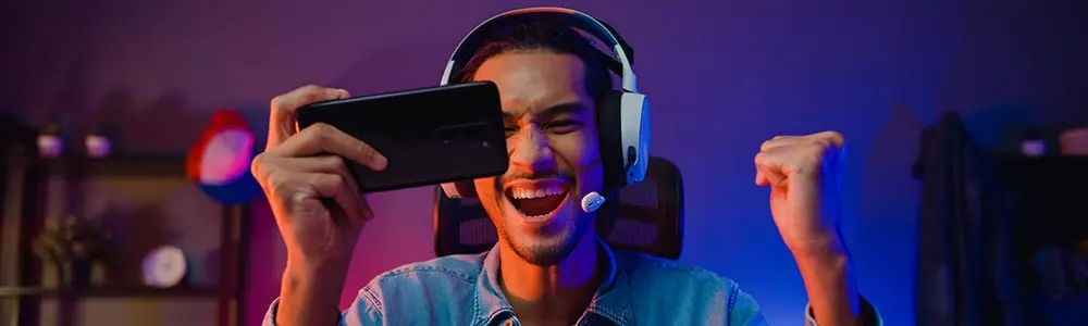 man wearing earphones celebrating a win on an online game on his phone.