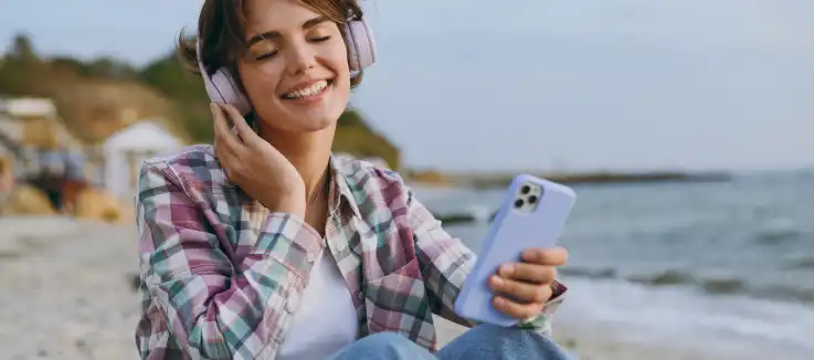 Woman sitting next to the ocean, holding a mobile phone 